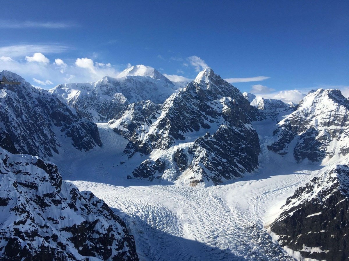 Snowy mountain peaks and a heavily crevassed glacier beneath a clear blue sky.