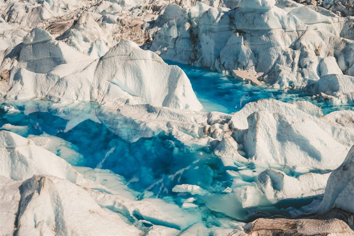 Bright turquoise melt pools surrounded by fractured white glacier ice.