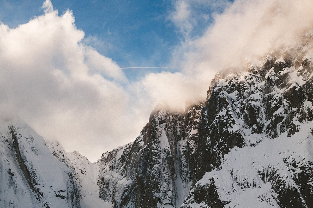 Snow-covered mountain walls rise into clouds beside a patch of blue sky.